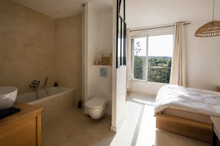 Chambre lumineuse avec salle de bain moderne attenante et grande fenêtre sur jardin verdoyant