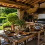 Table en bois dressée sous cuisine d'été extérieure couverte avec barbecue et plantes vertes